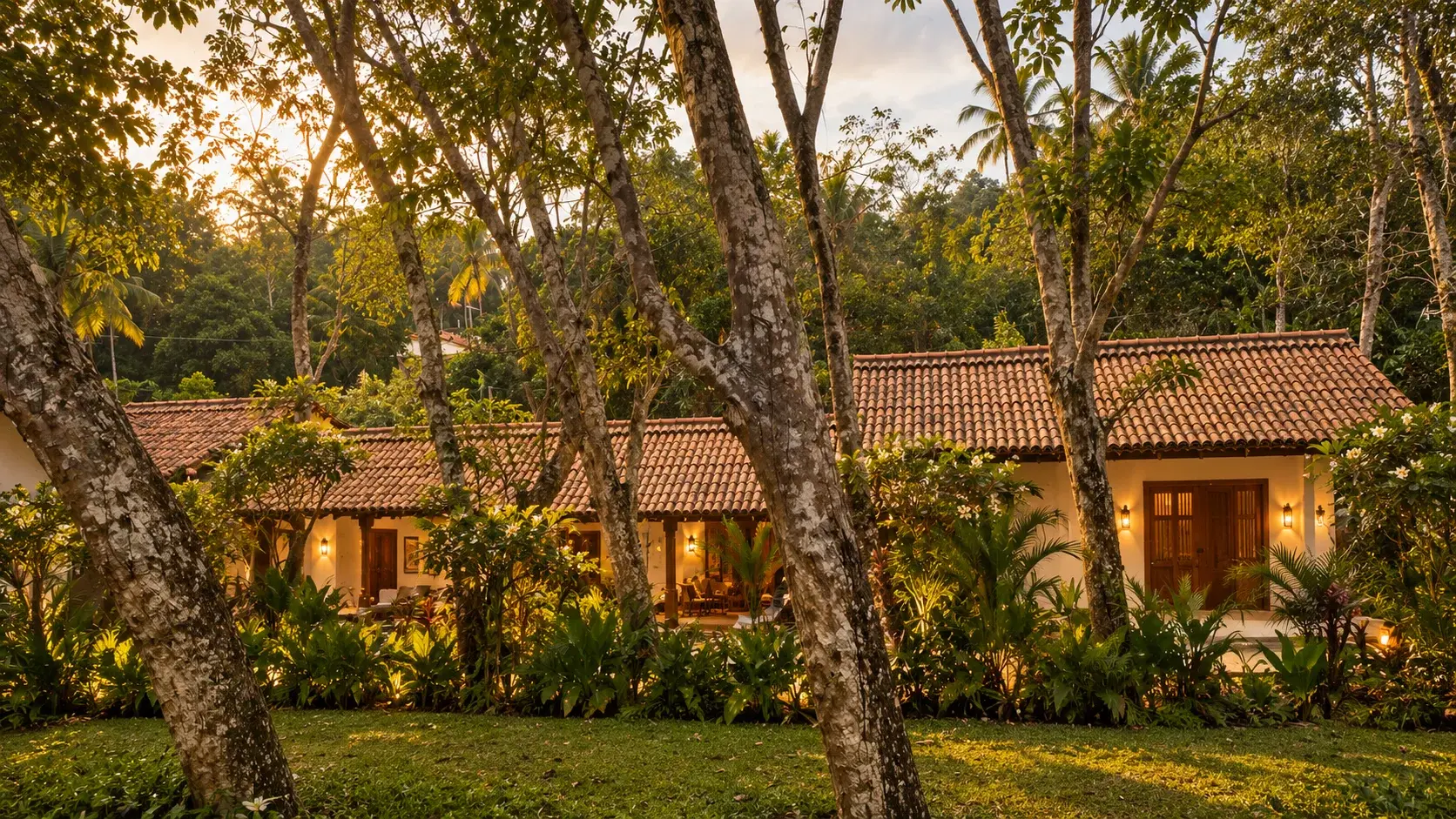 Colonial-era villa with a terracotta tiled roof, seen through tall trees at golden hour