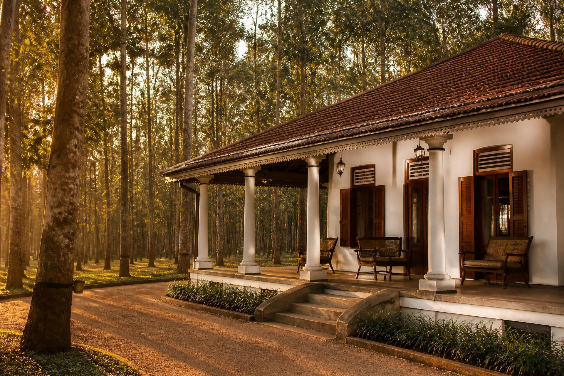 Colonial-era villa with a deep veranda set among rubber trees at golden hour