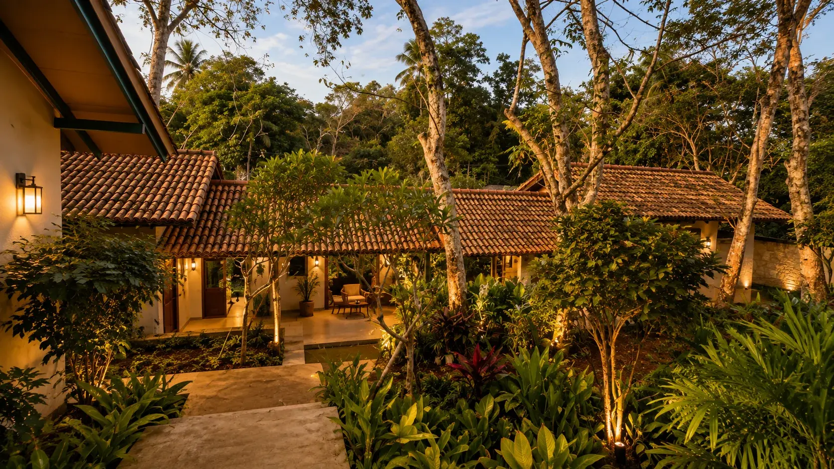 Tiled-roof reception building connected by an open walkway through the plantation, lit at dusk